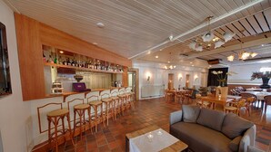 Amplia sala de estar con bar, diversas opciones de asientos, incluyendo un sofá y sillas, y piso de baldosas.