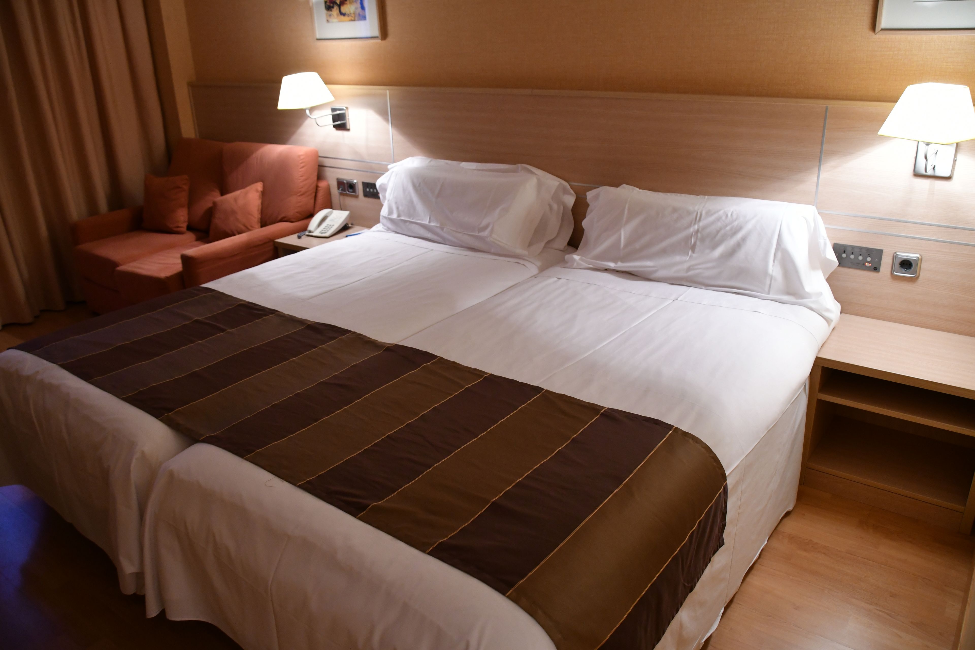 Habitación de hotel con una cama grande, dos mesitas de noche, una silla y una lámpara.