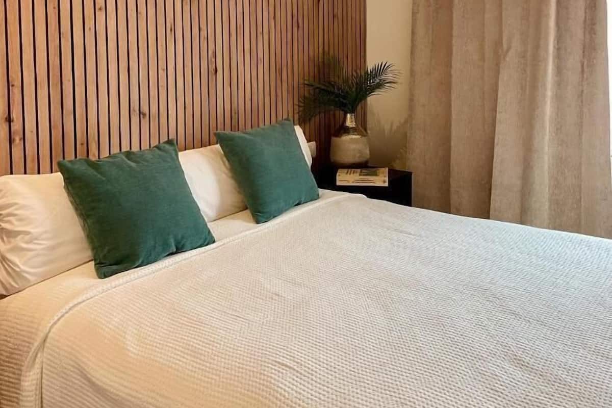 Een slaapkamer met een wand van houten latten, een bed met wit beddengoed en een nachtkastje met een plant.