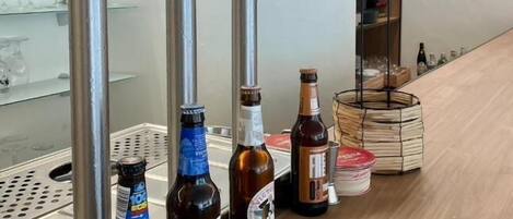 A bar area with a beer tap station, bottles of beer, and a shelf with various bottles.