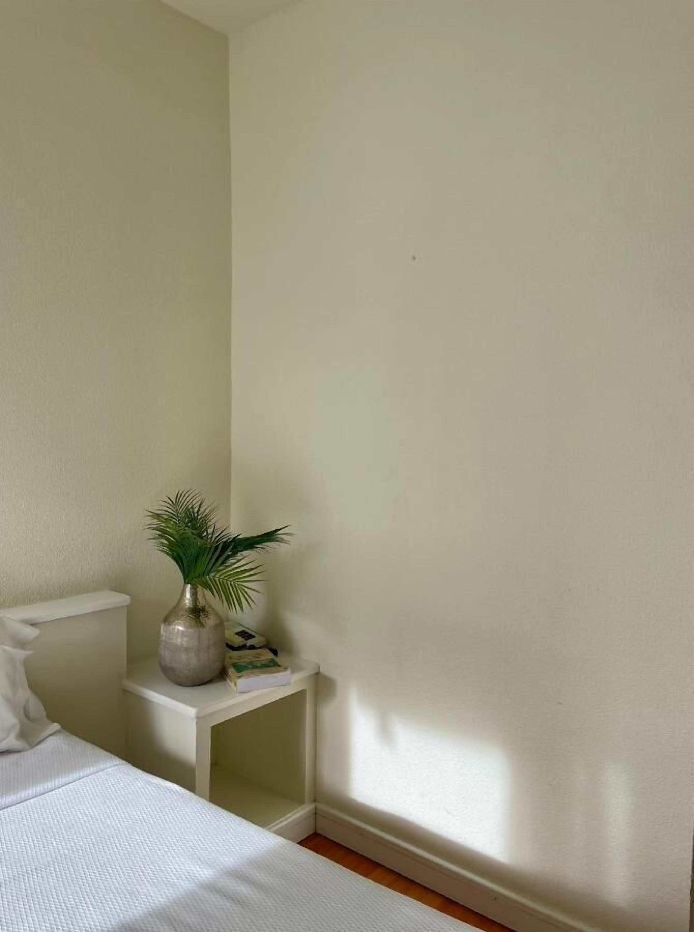 A bedroom with a bed, a nightstand, and a potted plant.