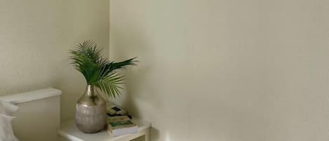 A bedroom with a bed, a nightstand, and a potted plant.