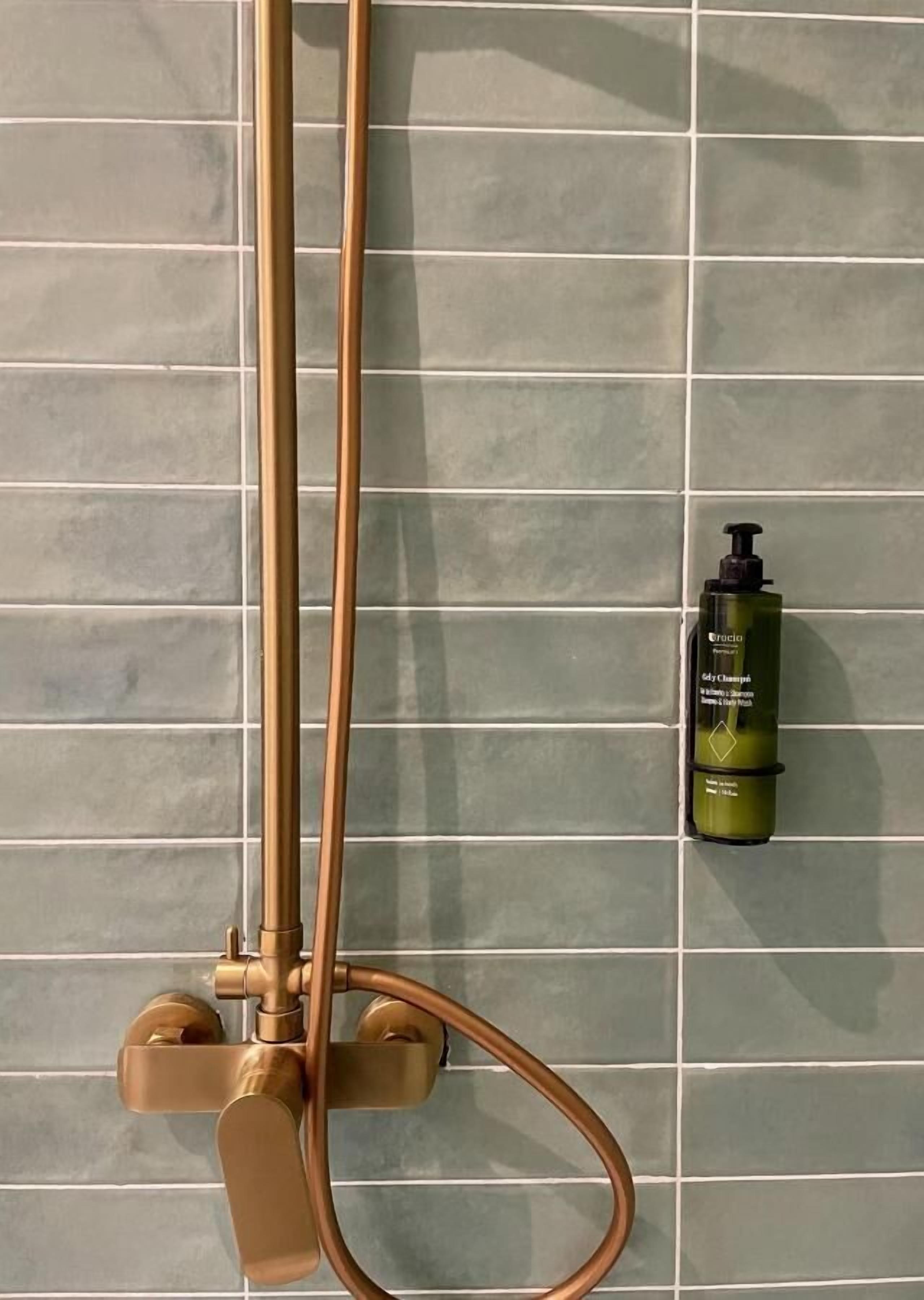 Ducha con grifo dorado y una botella de Crisco para el cuerpo sobre un muro con azulejos.