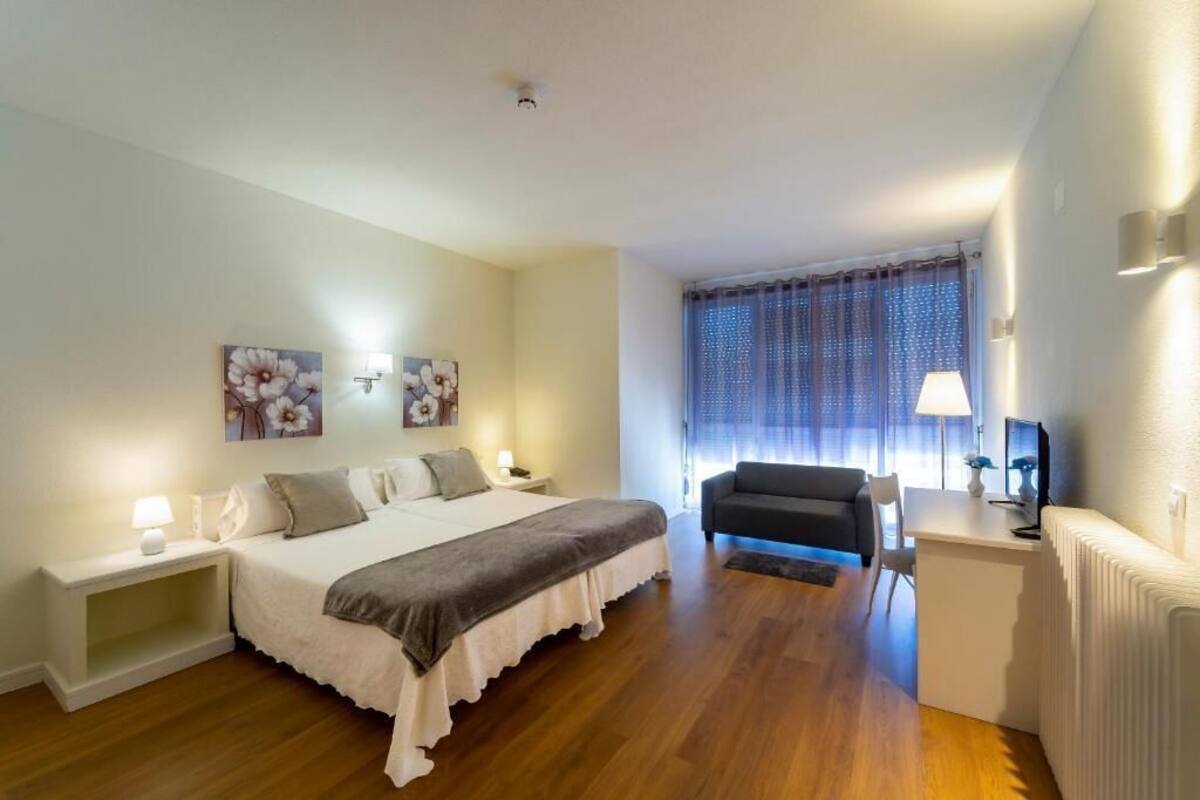 Een slaapkamer met een bed, nachtkastjes, een bureau, een stoel en een raam met gordijnen.