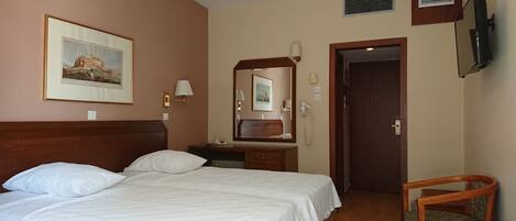 A hotel room with a double bed, a bedside table, a chair, a mirror, and a television mounted on the wall.