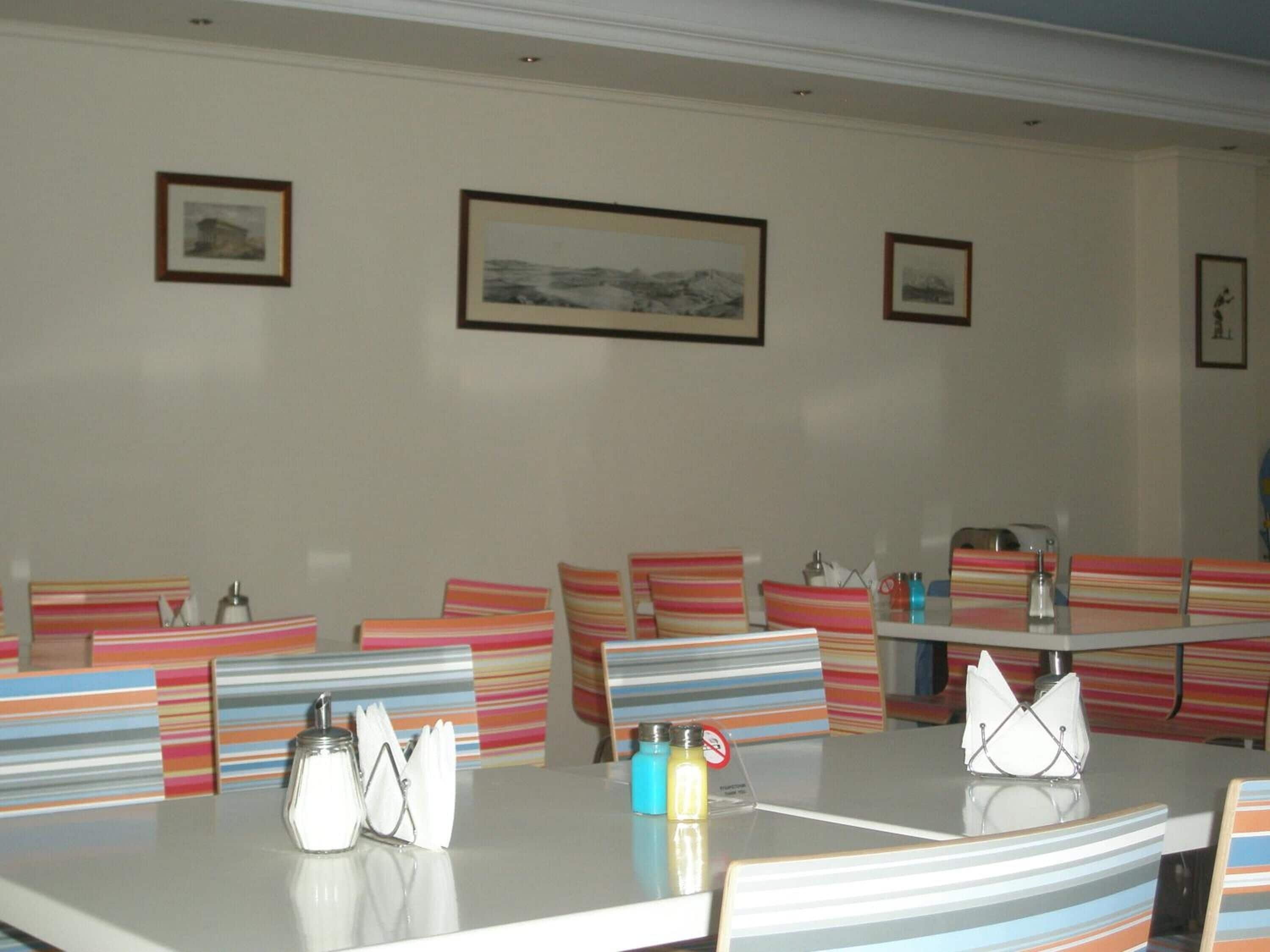 A dining area with striped chairs, a table with napkins, salt and pepper shakers, and framed pictures on the wall.