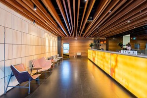 Guests can check in at the reception desk, surrounded by comfortable seating and a digital information kiosk.