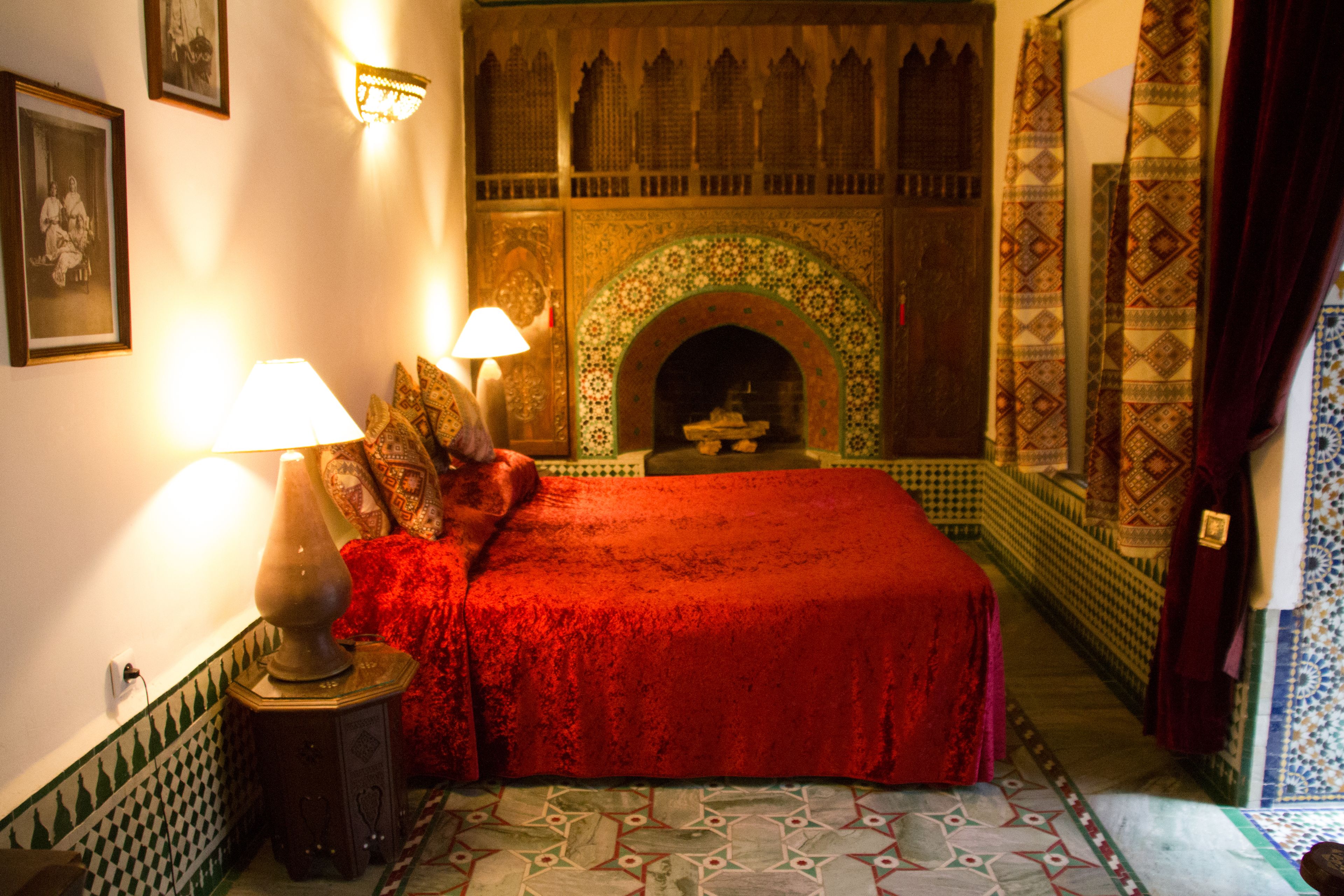 Una habitación con una cama grande, dos lámparas adosadas a la pared, una chimenea con diseño y un suelo de baldosas.