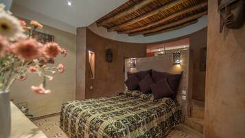A bedroom with a patterned bedspread, a wooden ceiling, and a decorative wall piece.