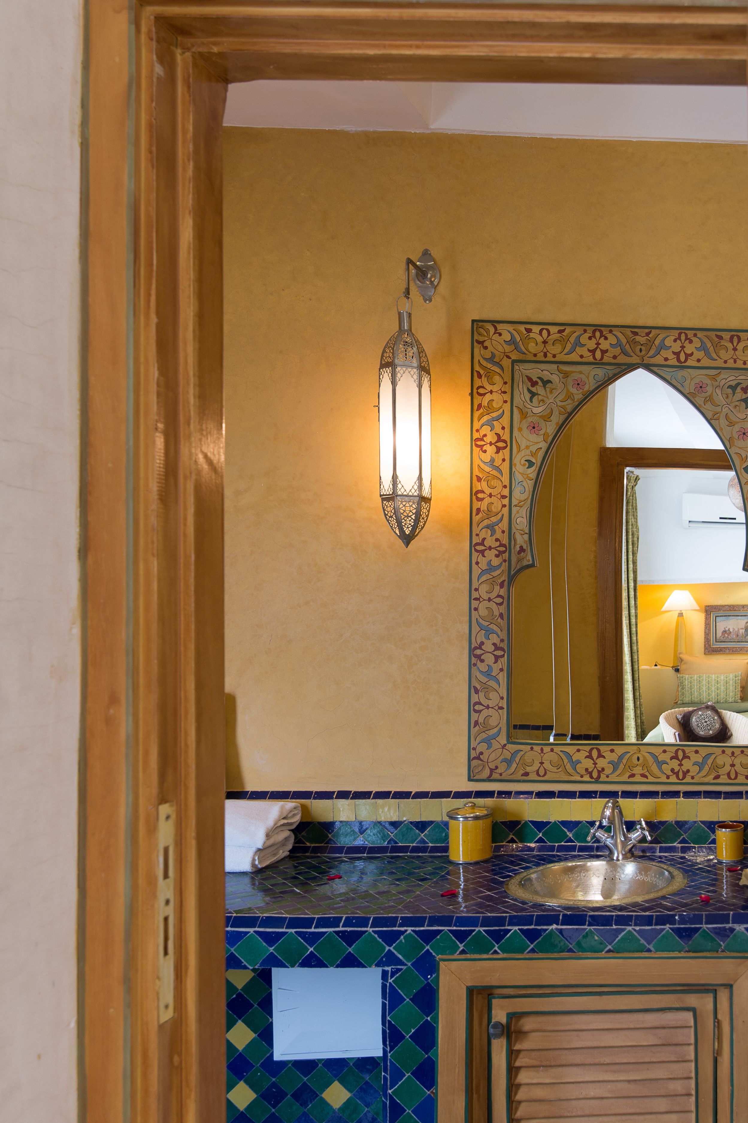 A bathroom with a tiled sink, a mirror with an ornate frame, and a wall-mounted light fixture.