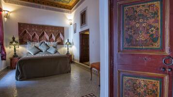 Una habitación tradicional con cama, mesitas de noche y un detalle decorativo en la pared.