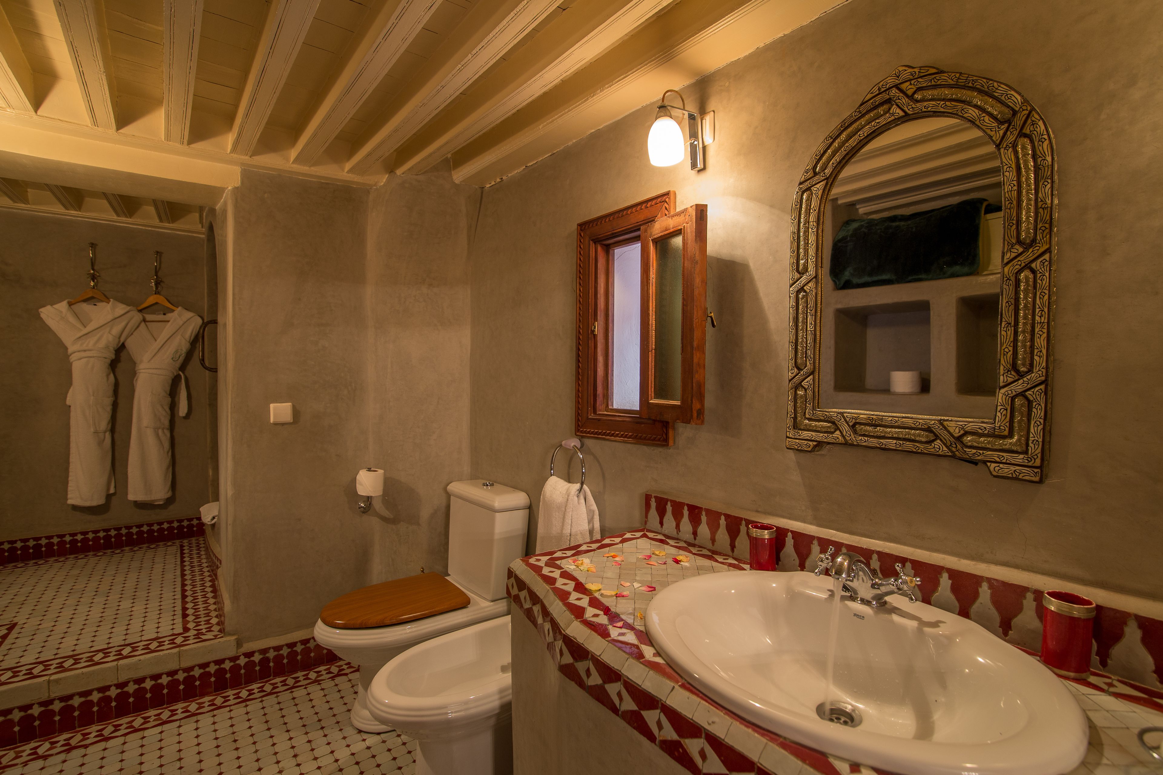 Un baño con un asiento de váter de madera, un lavabo blanco y un espejo con un marco decorativo.