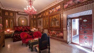 Una habitación ricamente decorada con paredes ornamentadas, un candelabro, una cama con ropa de cama roja y un sillón rojo.