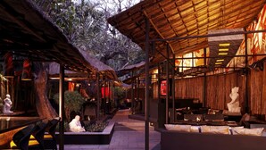 Un espace extérieur aménagé en restaurant, avec des toits de chaume, des tables et des chaises, ainsi que des statues décoratives.