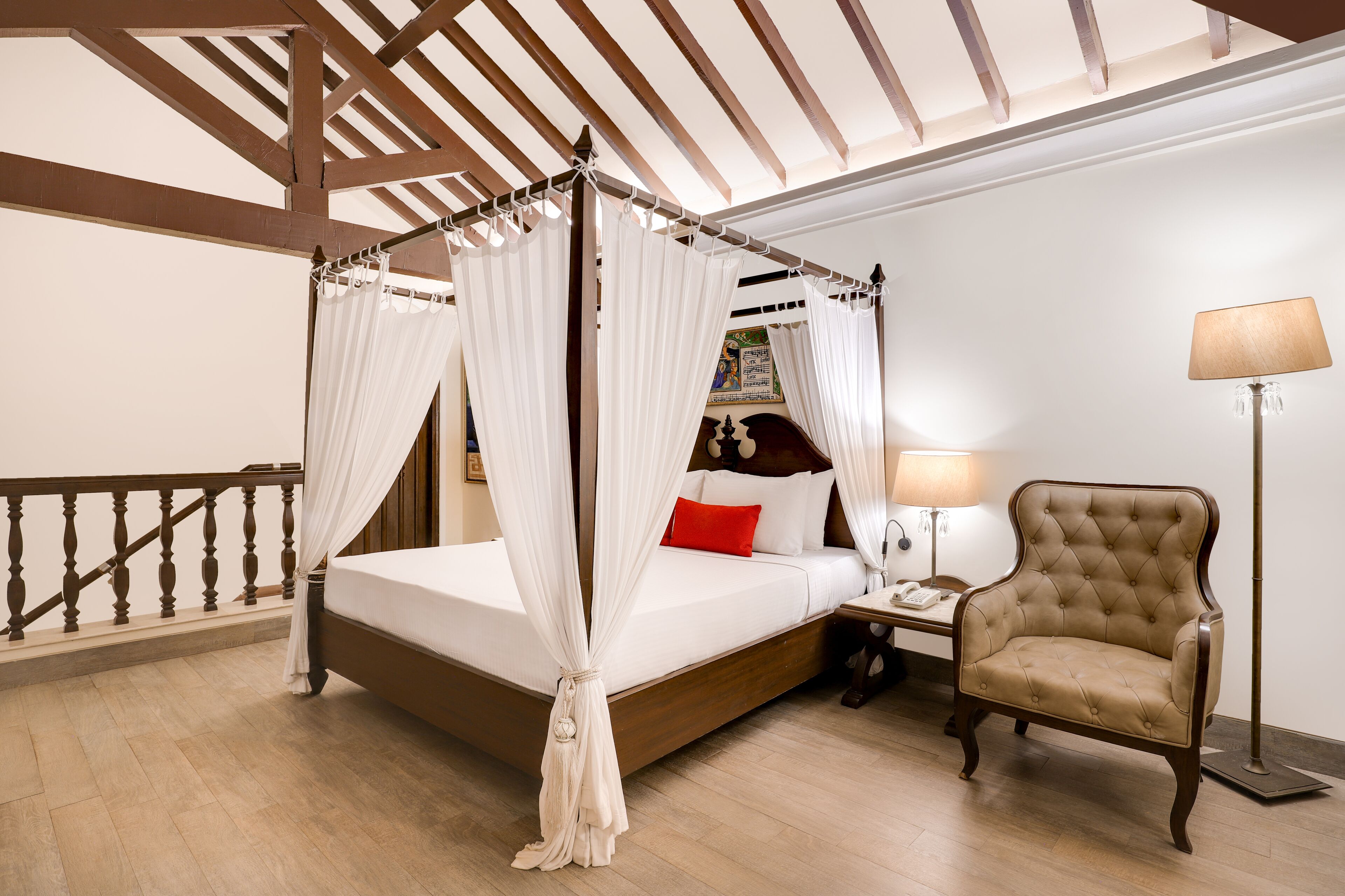 A four-poster canopy bed with a wooden headboard, a bedside table with a lamp, and a tufted armchair.