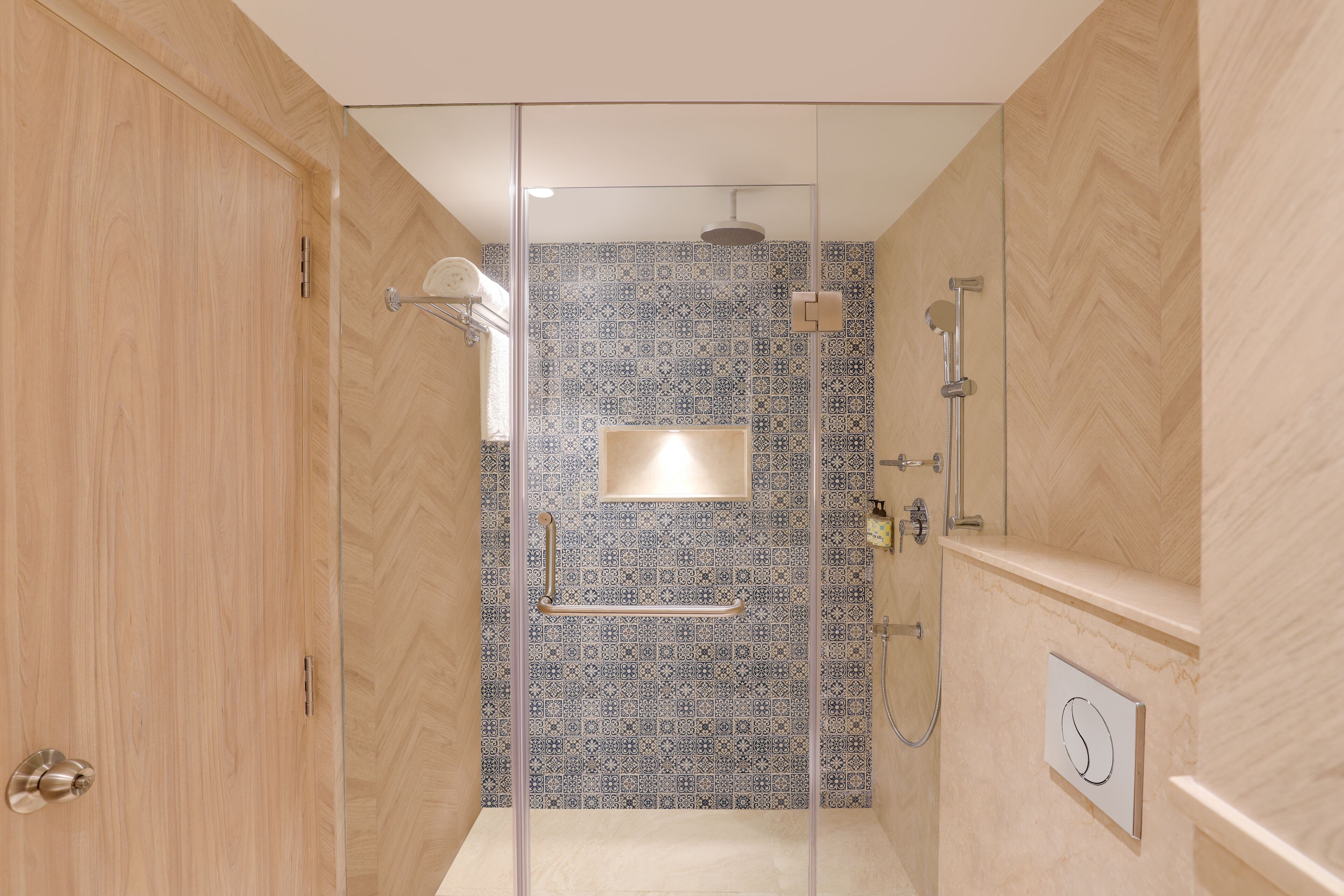 A modern bathroom with a glass shower enclosure, patterned tiles, and a wooden door.