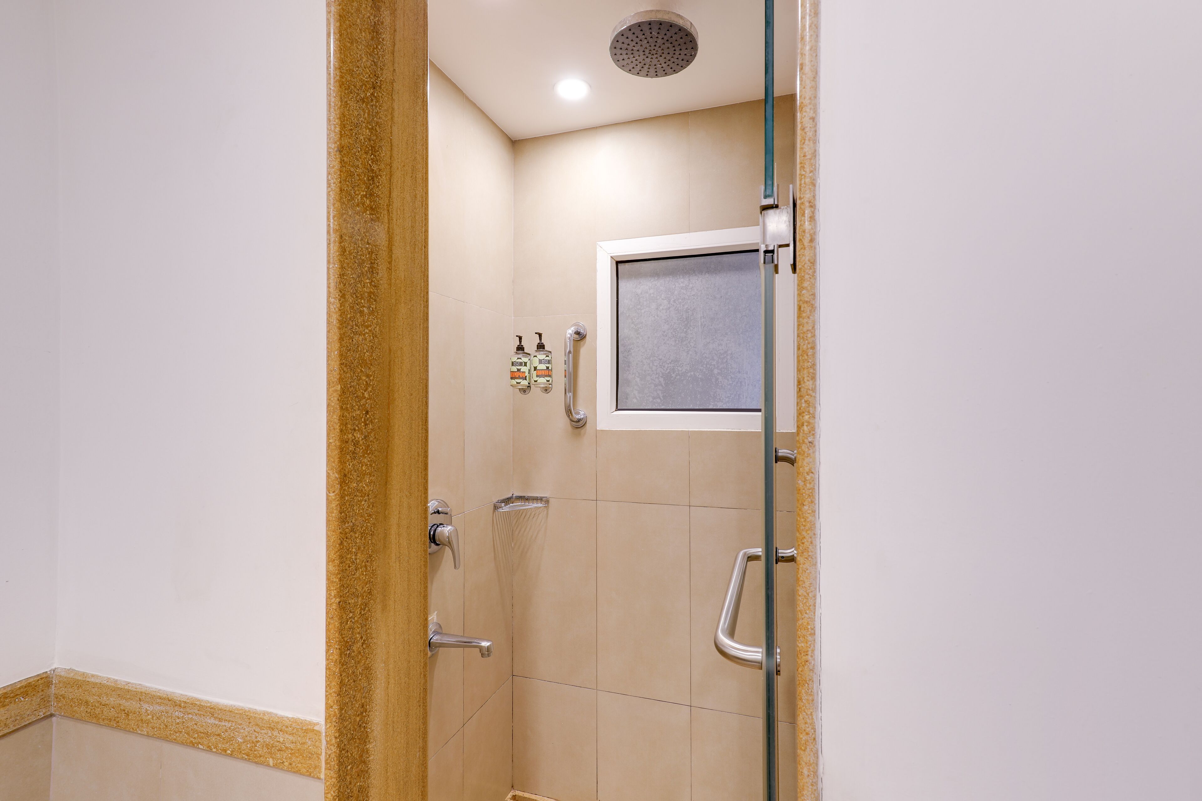 A shower with a glass door, a window, and hand sanitizer dispensers.