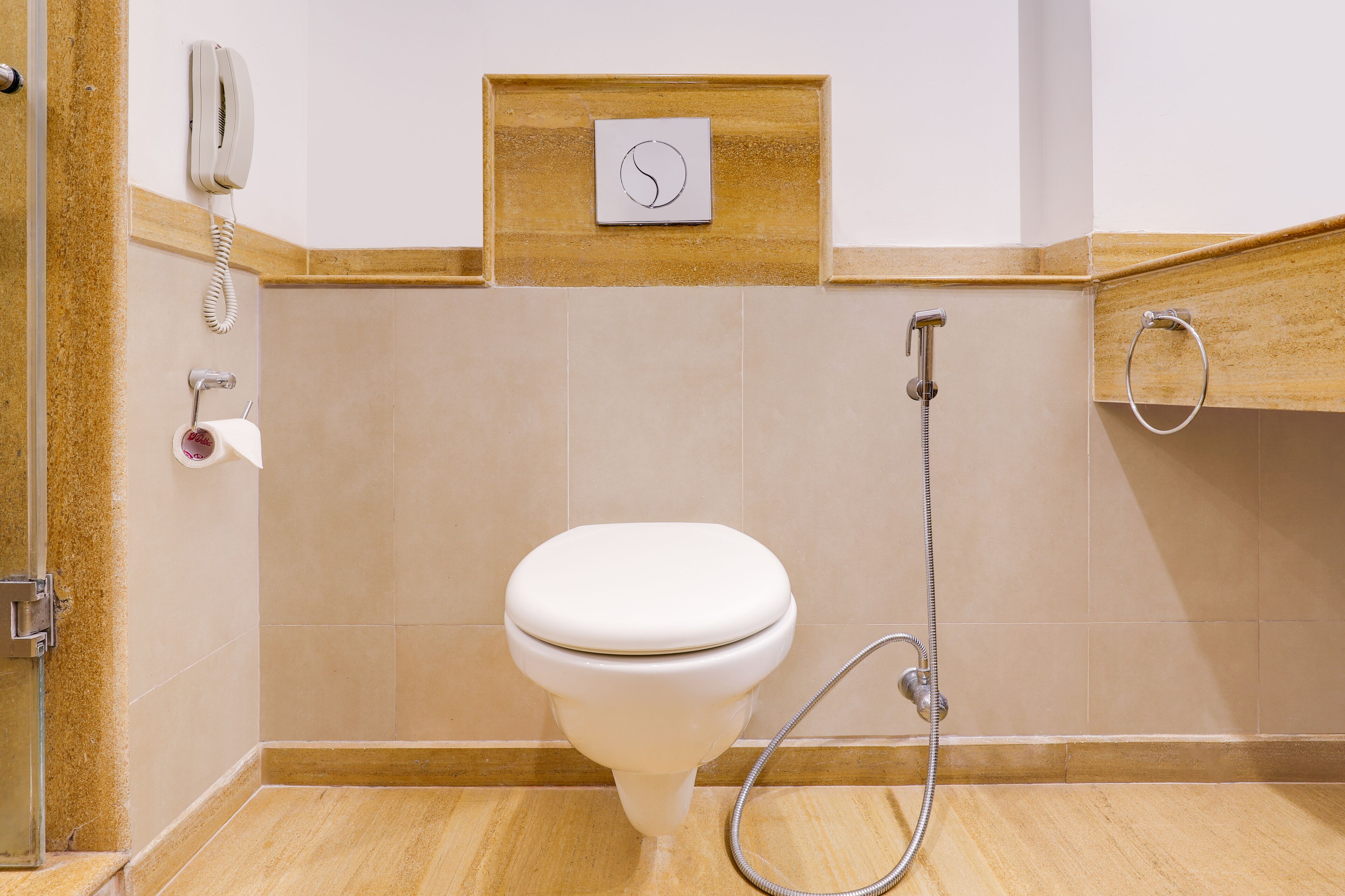 A bathroom with a toilet, a shower, and a telephone mounted on the wall.