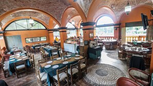 Ein Restaurant mit mehreren Tischen und Stühlen, Backsteinbögen und großen Fenstern.