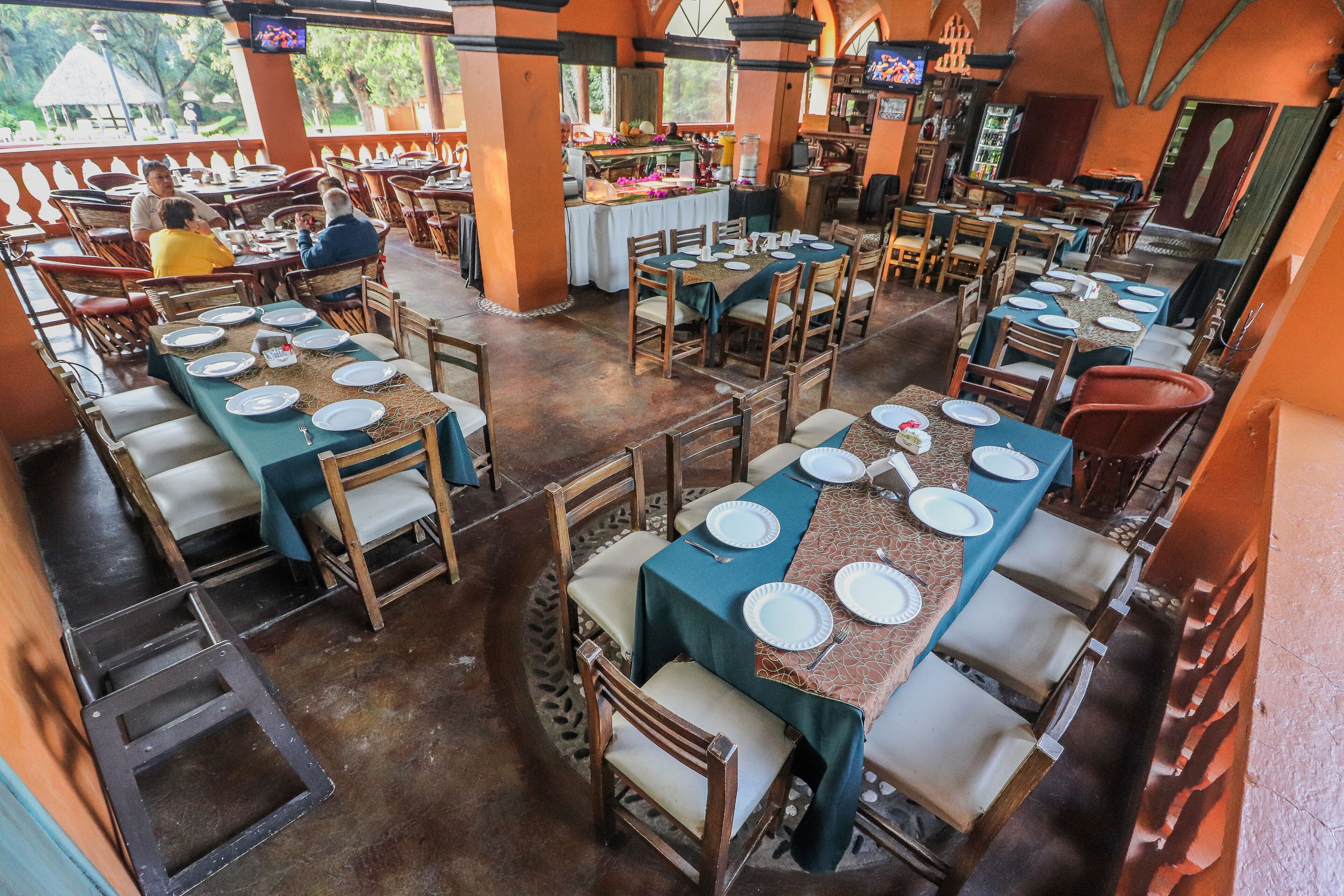 Un restaurante con varias mesas dispuestas, con platos y cubiertos, rodeado de sillas de madera.