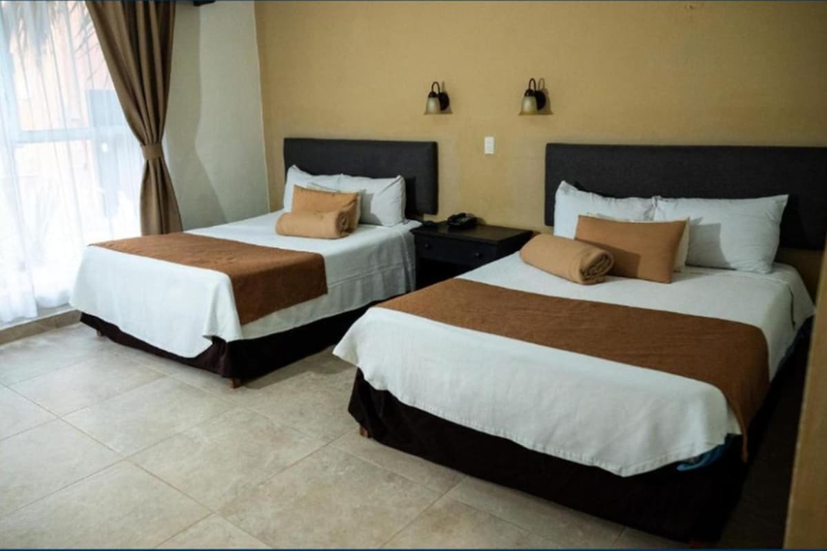 Two single beds with brown headboards and white bedding, a nightstand with a phone, and a window with curtains.