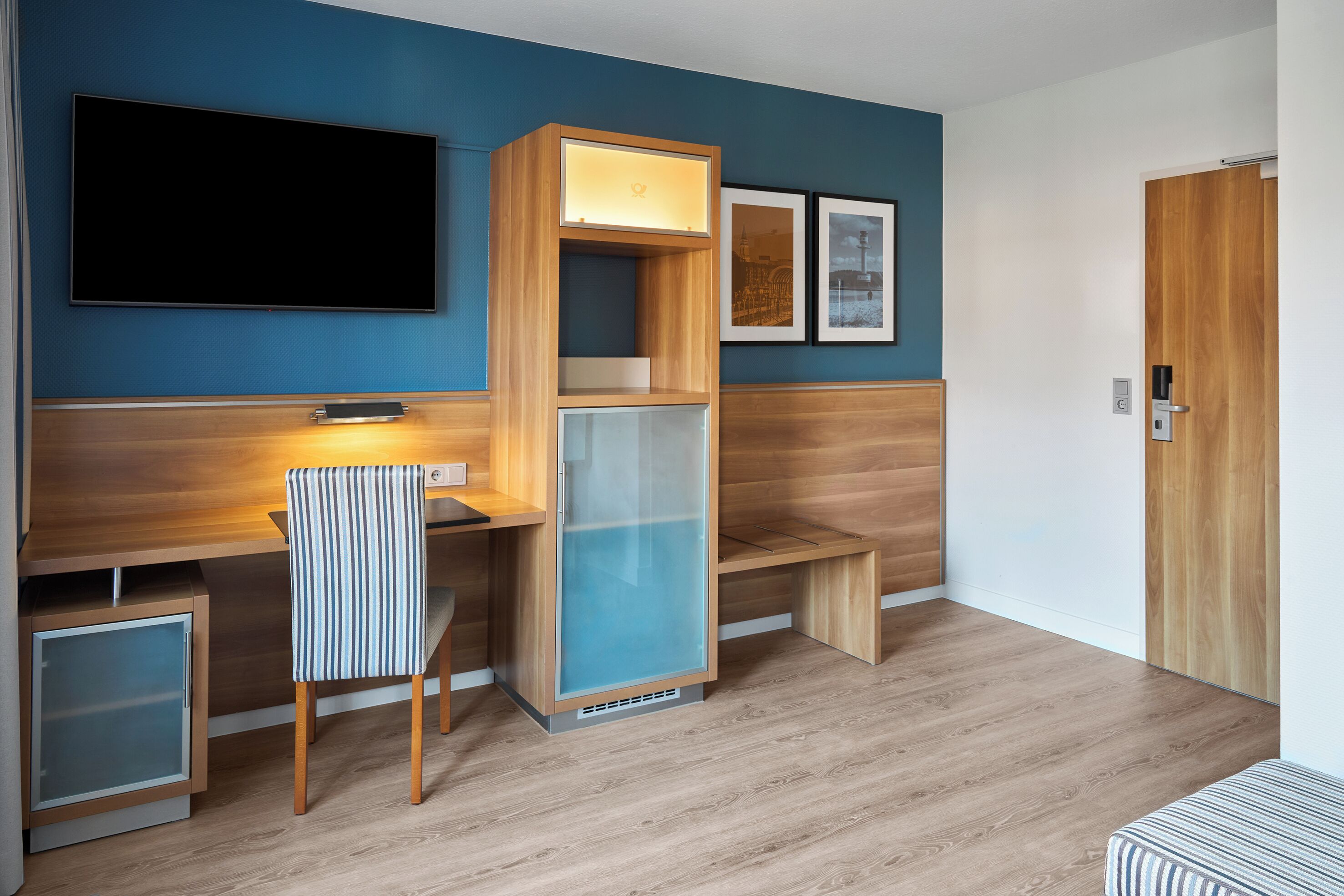 A modern room with a flat-screen TV, a wooden desk with a chair, a glass cabinet, and a bench.
