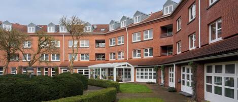 A row of red brick buildings with white windows, a covered outdoor seating area, and a well-maintained lawn.
