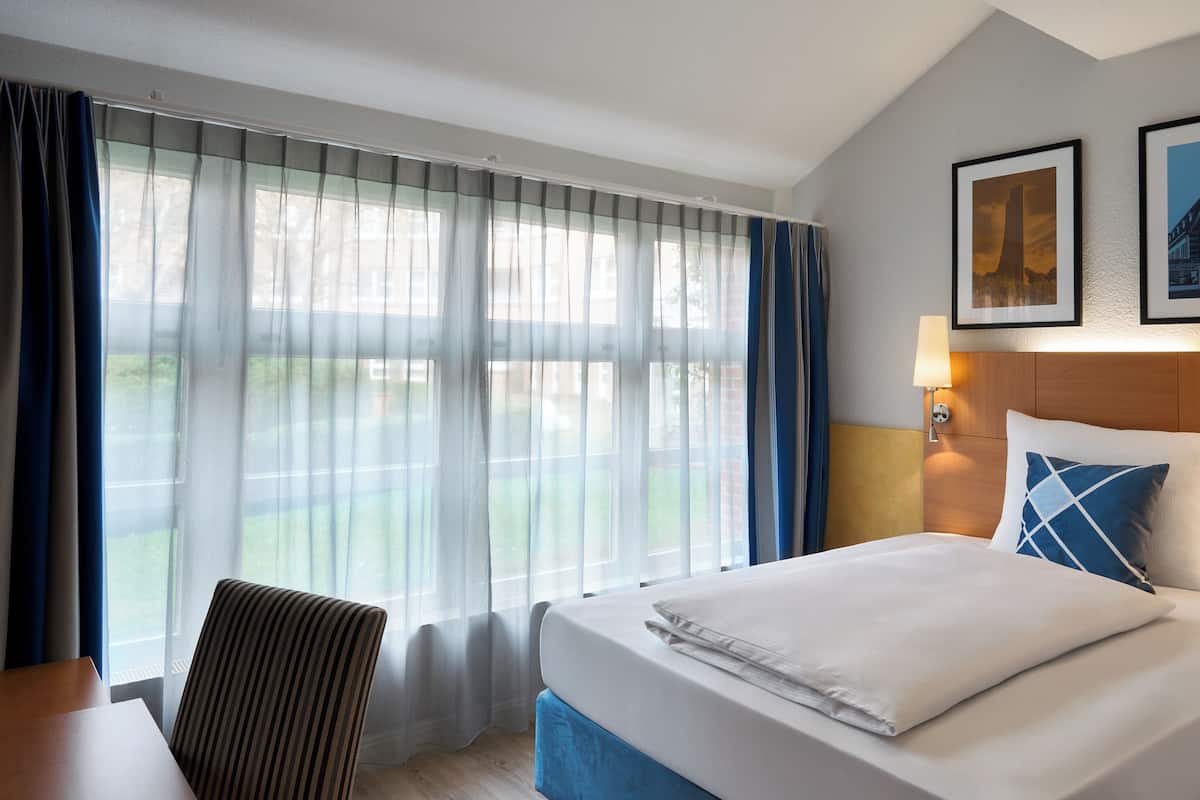 Una habitación de hotel con cama, una silla, un escritorio y vistas por la ventana.