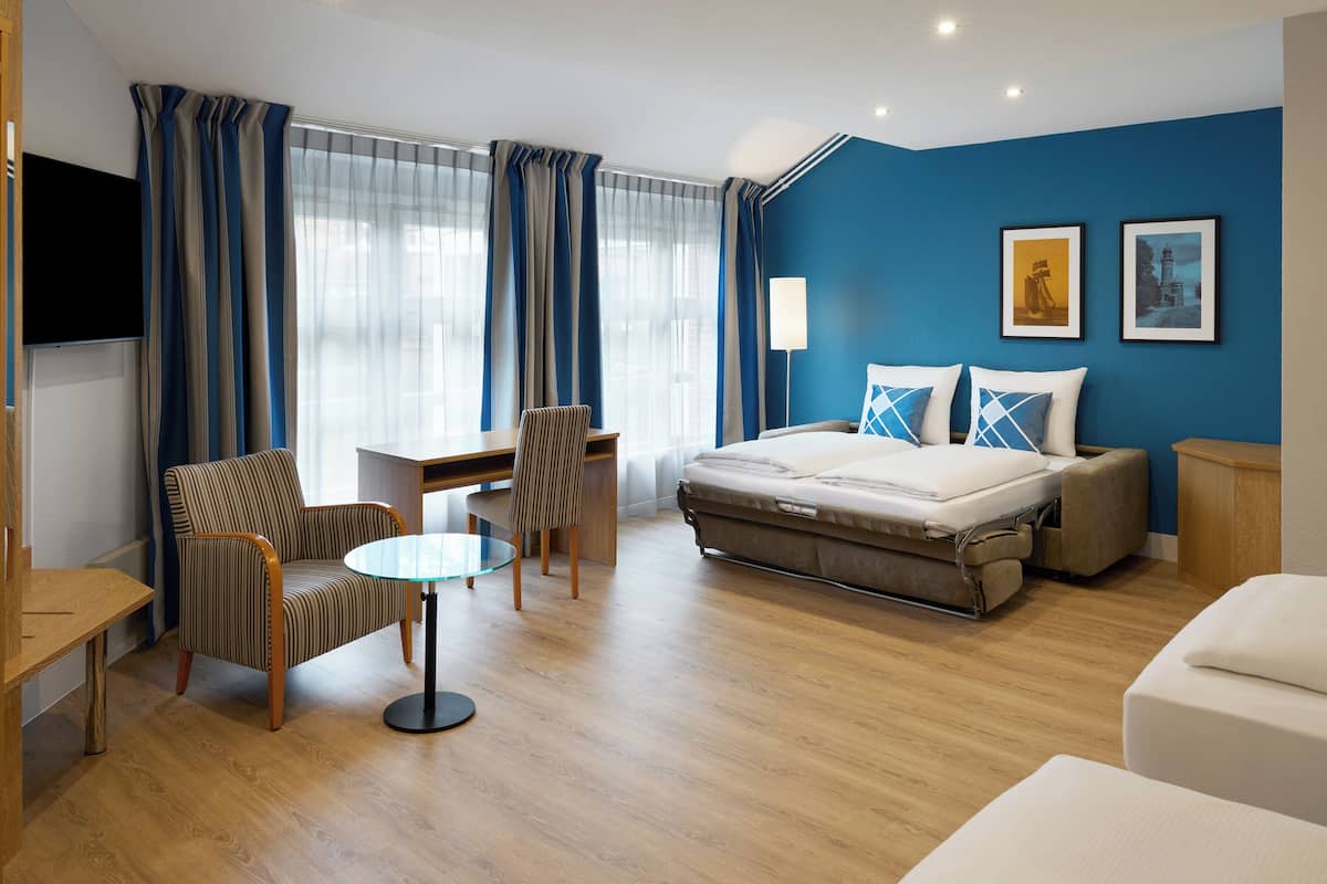 Una habitación de hotel con una cama, un escritorio, una silla, una mesita y un televisor.