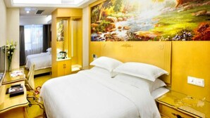 A hotel room with a large bed, a desk with a chair, a painting of a landscape on the wall, and a window with curtains. - GreenTree Inn Guangdong Shenzhen Dongmen Business Hotel (Shenzhen)