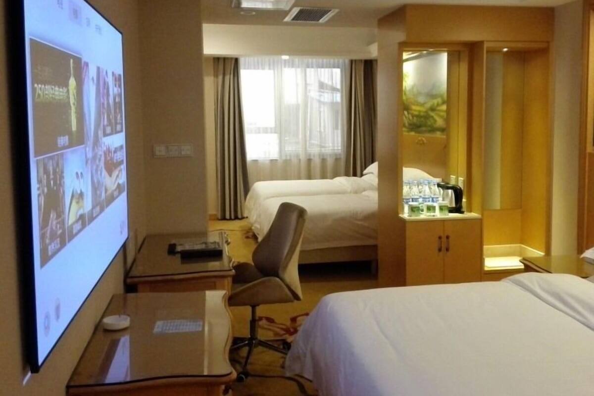 A hotel room with a bed, a desk with a computer, a chair, and a wardrobe.