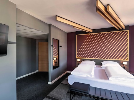 A modern hotel room with a large bed, bedside tables, a flat-screen TV, and a unique geometric wall design.