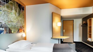 A hotel room with a bed, a desk, a mirror, and a wall with a cityscape mural. - B&B Hotel München-Hbf (Munich)