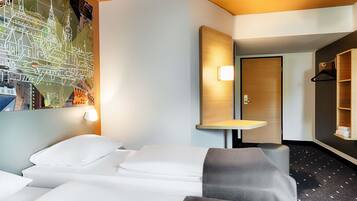 A hotel room with a bed, a desk, a mirror, and a wall with a cityscape mural.