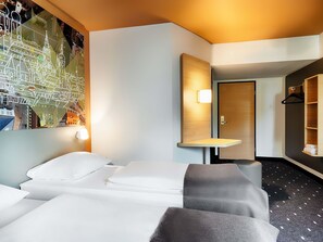 A hotel room with a bed, a desk, a mirror, and a wall with a cityscape mural. - B&B Hotel München-Hbf (Munich)