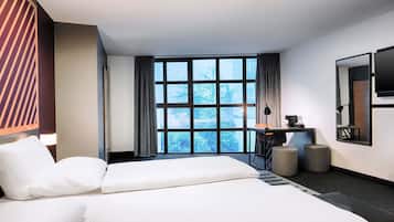 A modern hotel room with two beds, a desk, a chair, a TV, and a large window with a view of trees.