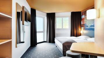 Ein Hotelzimmer mit Bett, Schreibtisch, Stuhl, Fernseher und einem Fenster mit Vorhängen.