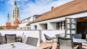 An outdoor patio with tables and chairs, a view of a church with a clock tower, and a building with large windows. - B&B Hotel München-Hbf (Munich)