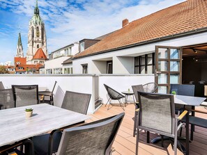 An outdoor patio with tables and chairs, a view of a church with a clock tower, and a building with large windows. - B&B Hotel München-Hbf (Munich)
