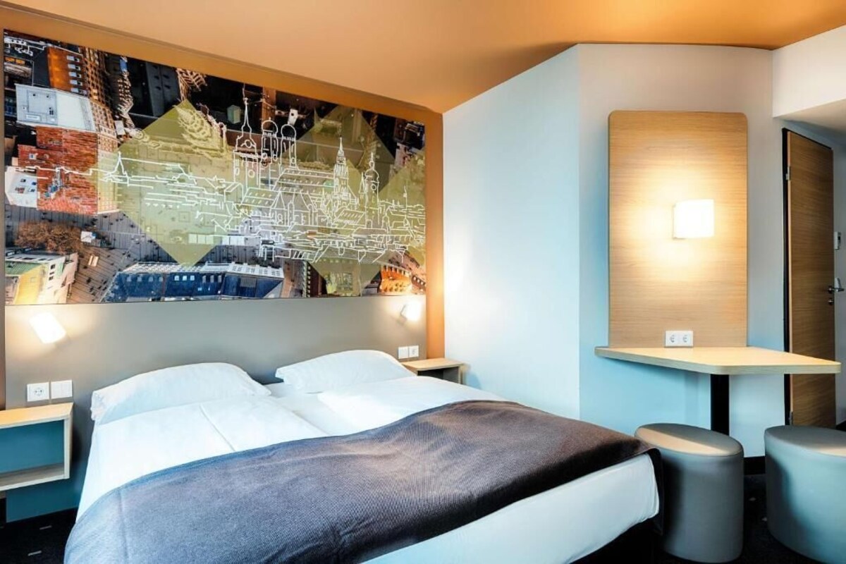 Une chambre d’hôtel moderne avec un grand lit, une carte accrochée au mur, une petite table et deux tabourets.