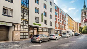 A hotel with a reception area, multiple floors, and a church in the background. - B&B Hotel München-Hbf (Munich)