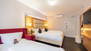 Een hotelkamer met twee bedden, een rode bank, een klein tafeltje met een bloevas en een houten kast.