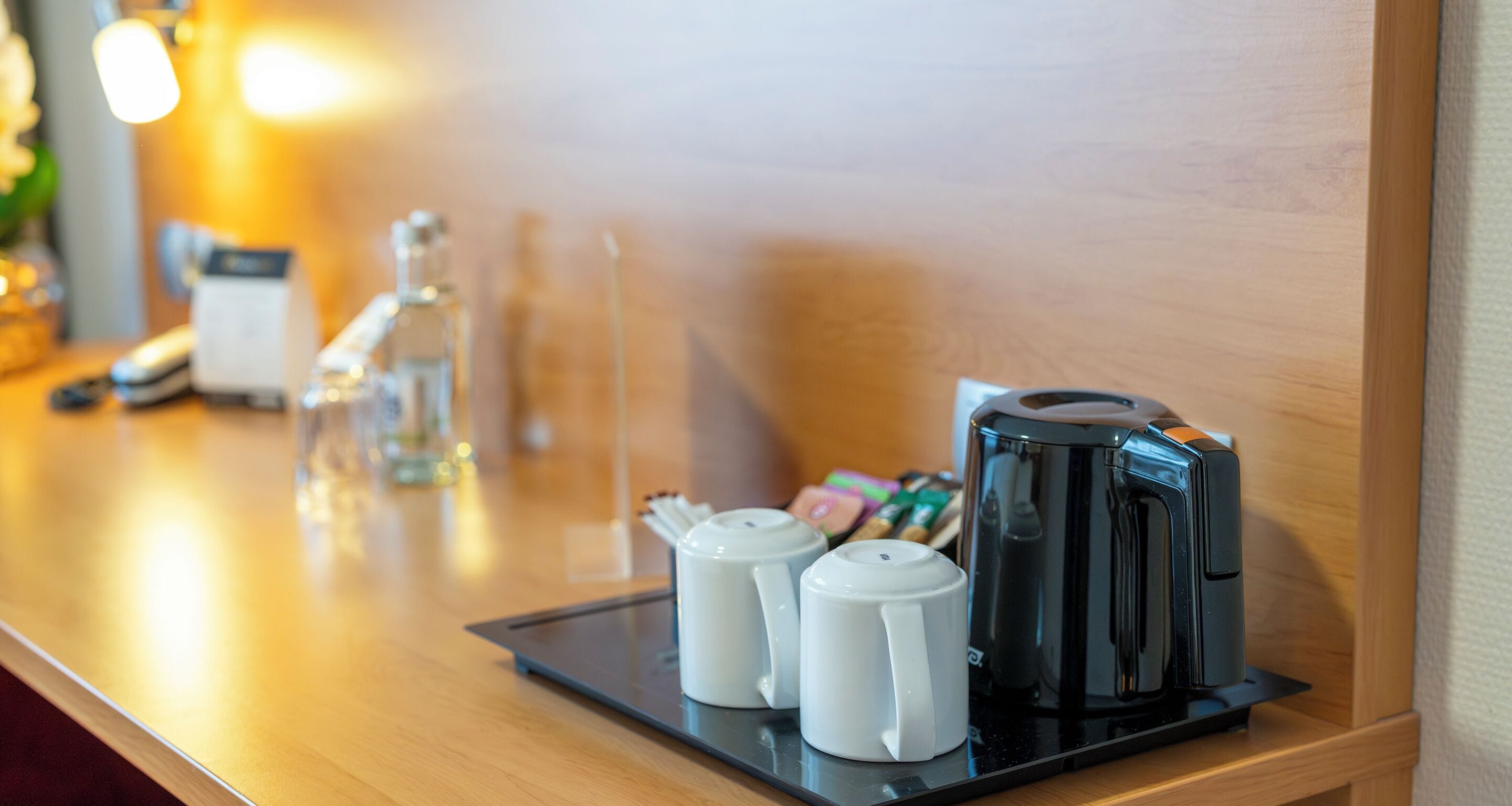 Un coin café comprenant une machine à café noire, deux sucriers blancs et un verre d’eau, le tout disposé sur un plateau.