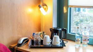 Une chambre d’hôtel avec un bureau en bois, une machine à café, deux tasses blanches, un pichet en verre et deux bouteilles d’eau.