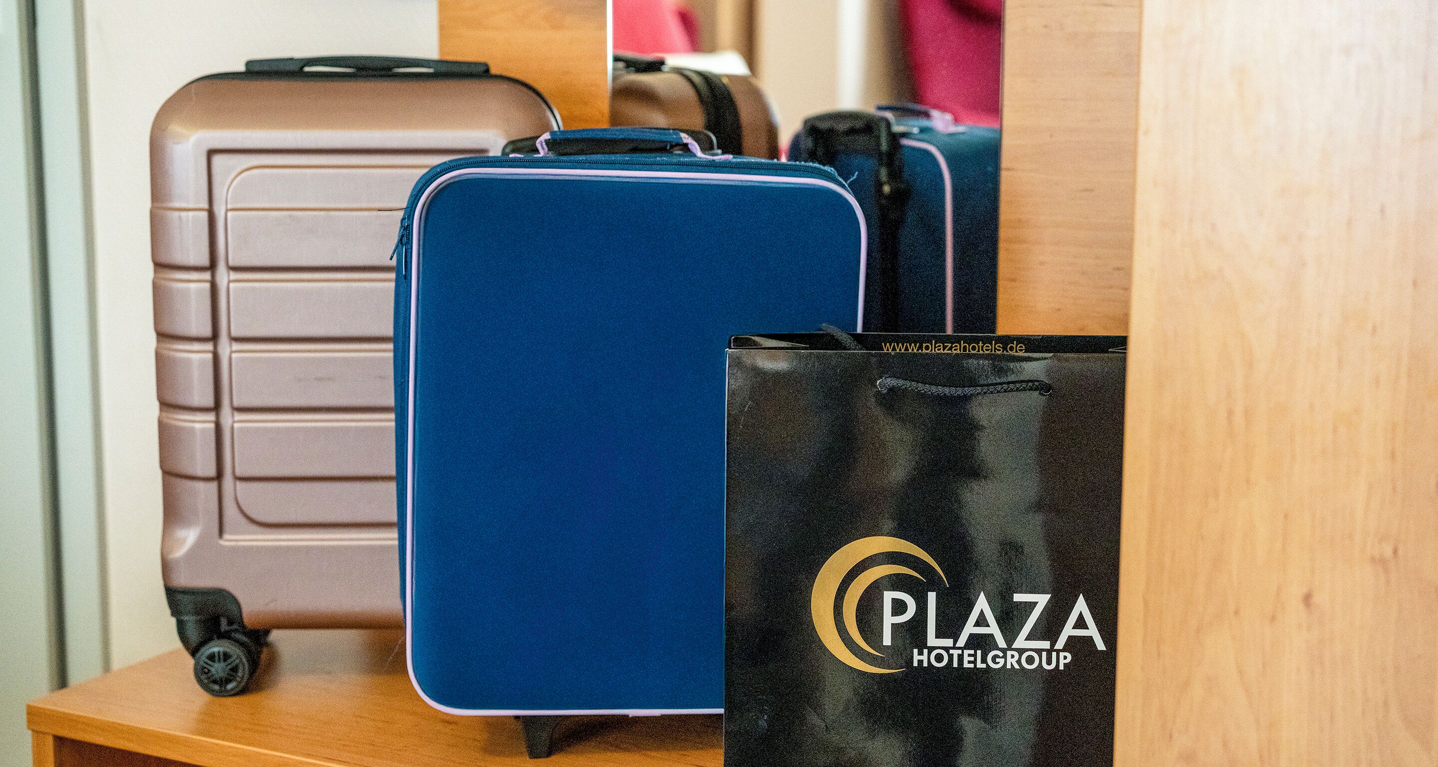 Een blauwe koffer, een bruine koffer en een zwarte tas met het logo van 'Plaza Hotelgroup' op een houten ondergrond.
