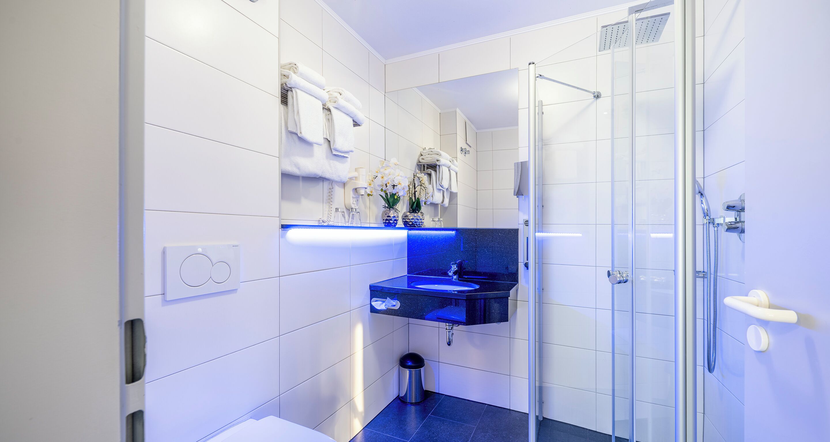 A modern bathroom with a glass shower enclosure, a black sink, and white tiled walls.