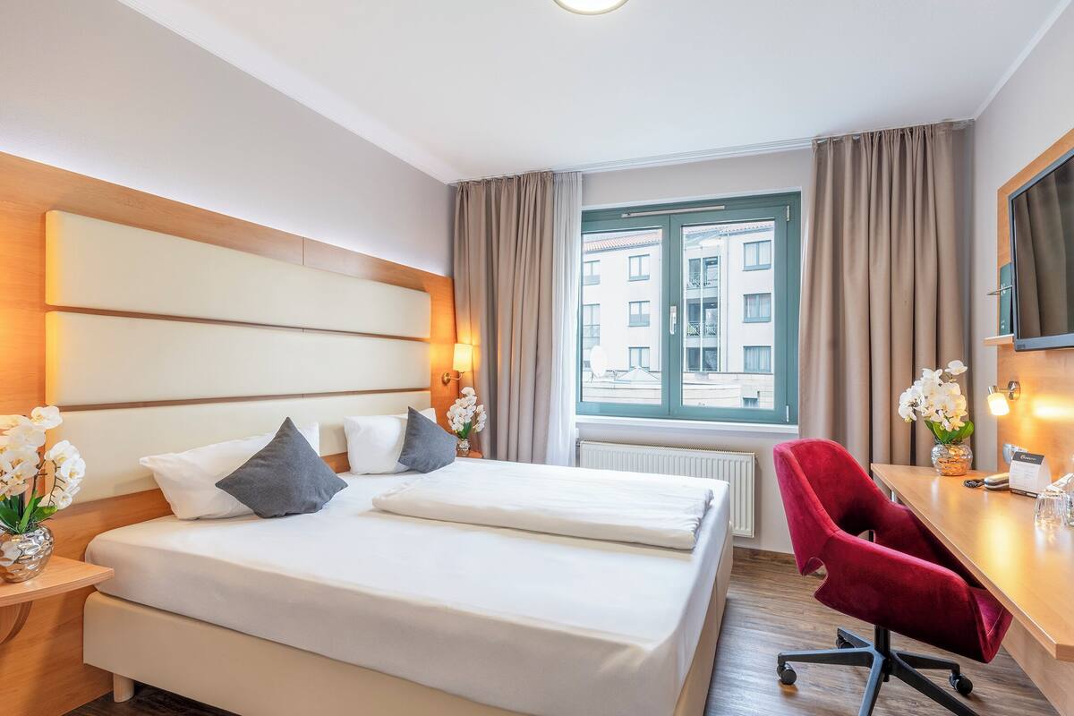 Una habitación de hotel con una cama, un escritorio, una silla y un televisor.