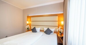 Una habitación de hotel con una cama grande, dos mesitas de noche y una mesita de noche con lámpara.