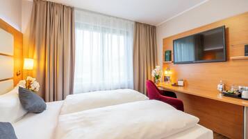 Une chambre d’hôtel avec deux lits, une télévision, un bureau avec une télécommande et une fenêtre avec des rideaux.