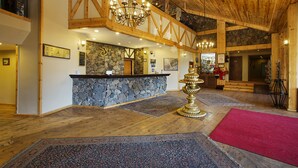 Un hall d’entrée spacieux avec un mur en pierre, des poutres en bois, un lustre et un comptoir d’accueil.